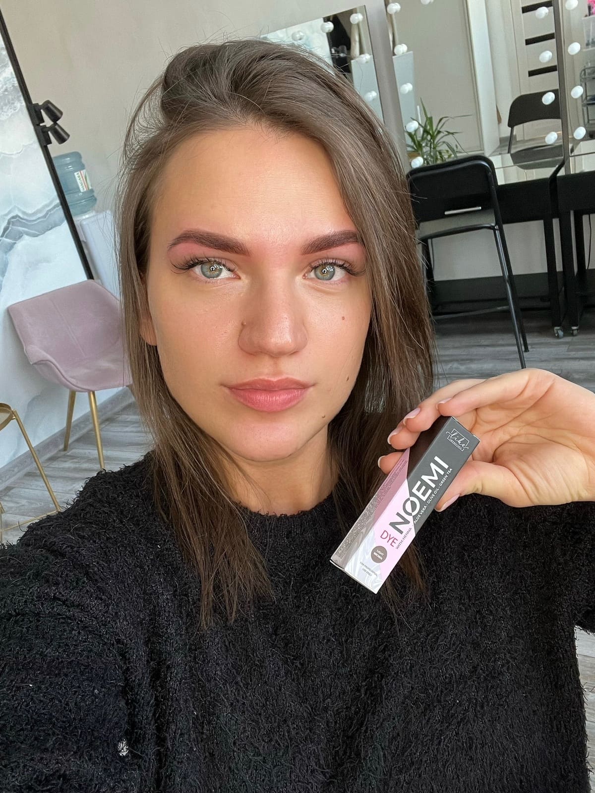 Female holding a tube of Noemi Dye light brown and showing her brows.